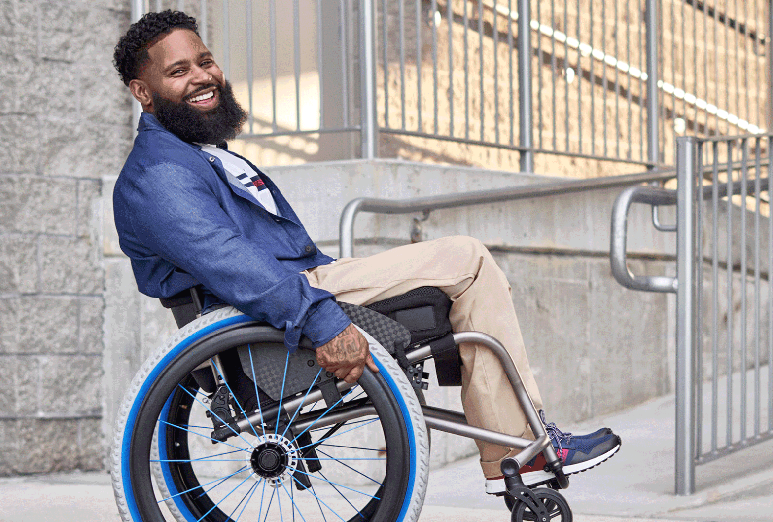 Wes doing a wheely in his wheelchair wearing a blue sport coat and khaki pants provided by Tommy Hilfiger for the IMIXX adaptive fashion event.